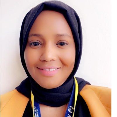 Smiling person wearing a black headscarf and yellow blazer against a white background.