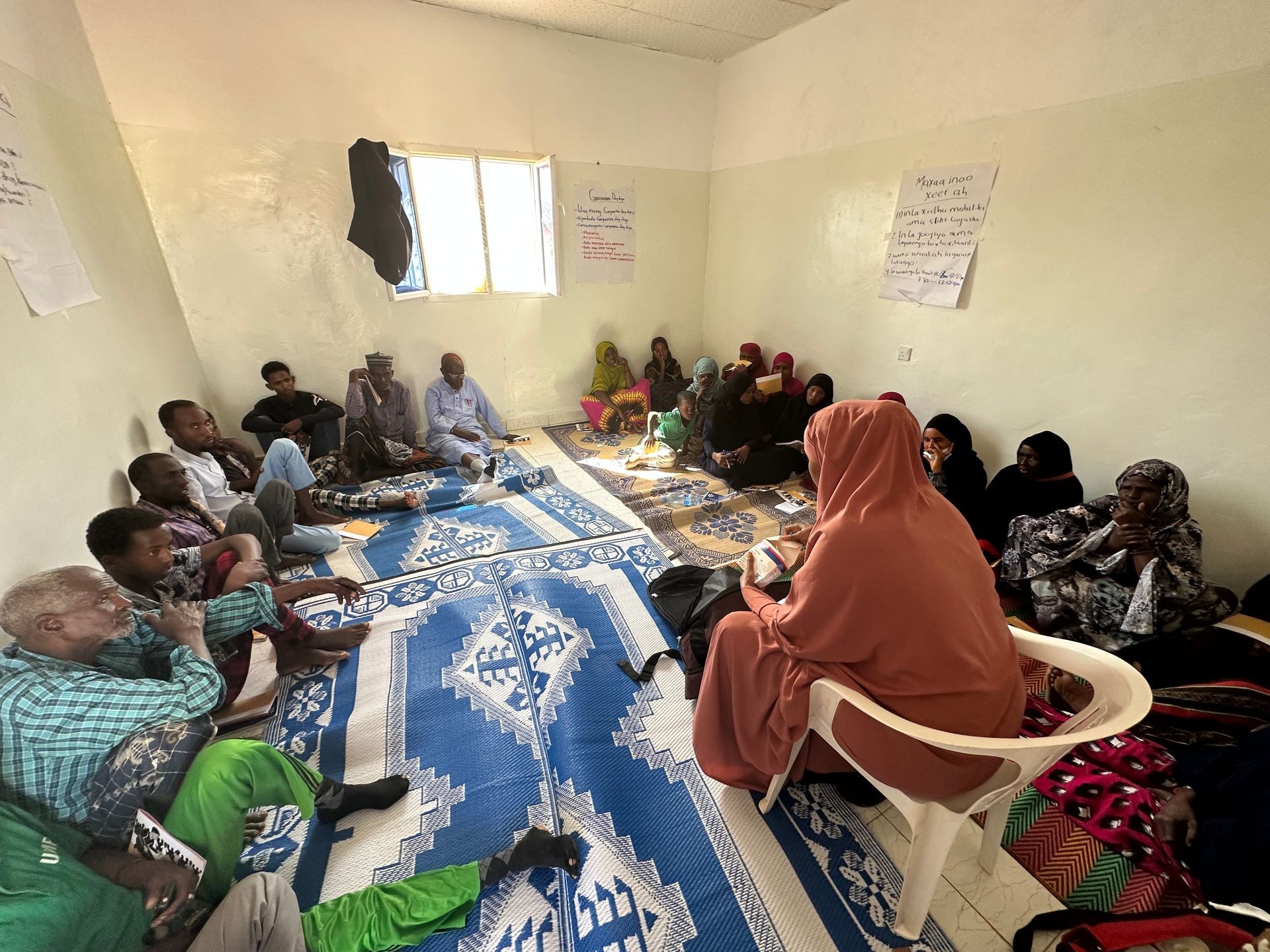 A group of people sitting on mats in a room, gathered for a meeting or discussion.