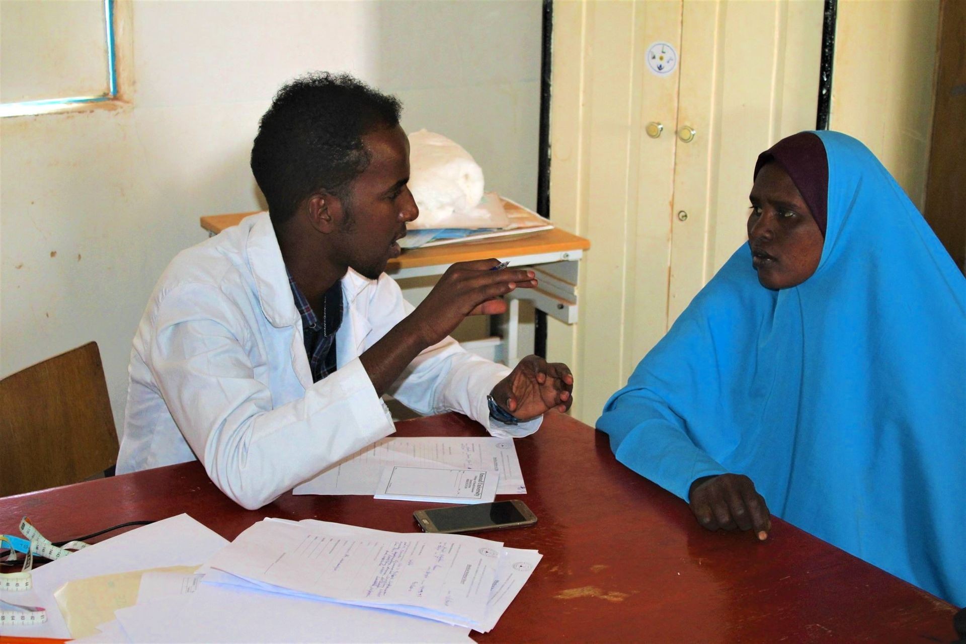 Doctor consulting with a patient in a medical office, with papers and a smartphone on the table.