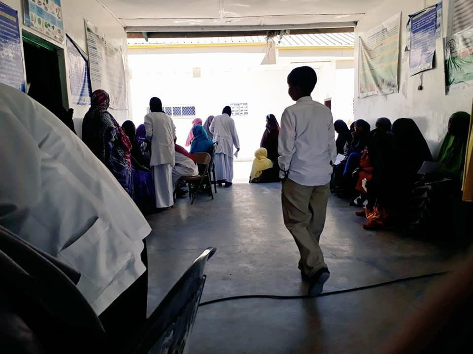 People sitting in a healthcare clinic waiting area, with some standing and engaging with medical staff.