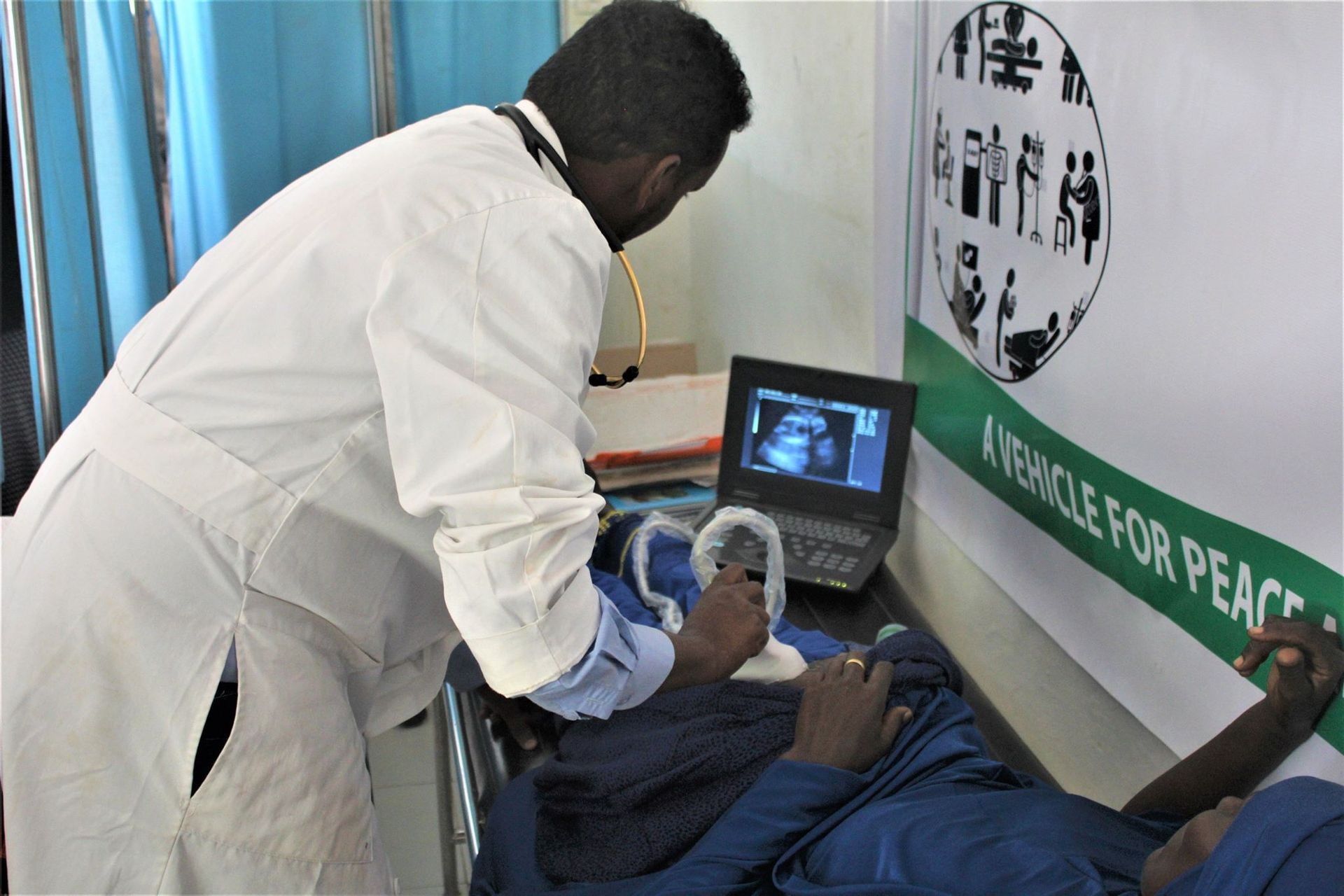 Doctor in a white coat performing an ultrasound on a patient's abdomen using a portable ultrasound machine.