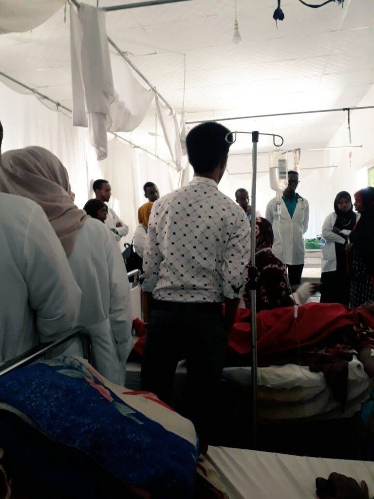 A group of people in a medical setting standing near hospital beds and equipment.